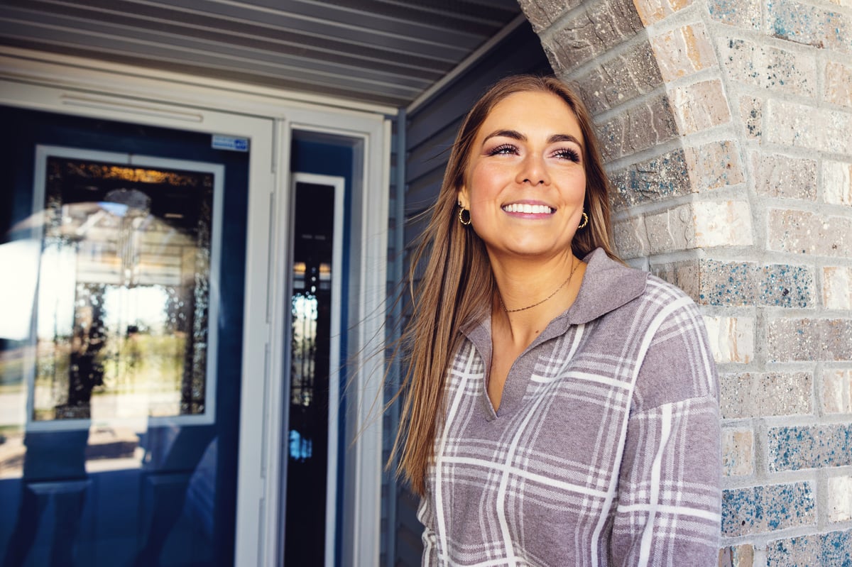 Girl with long brown hair standing in a brick doorway smiling