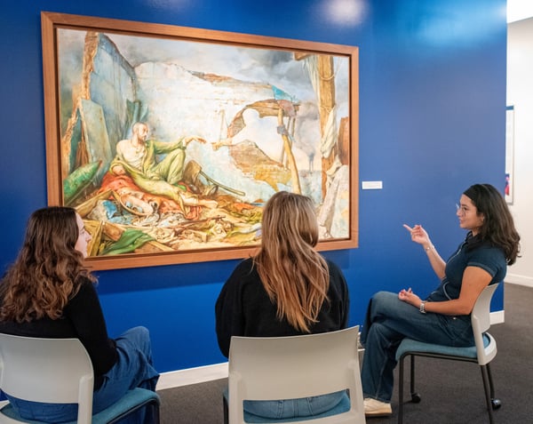 College students sitting in the Samuel Bak Musuem: The Learning Center looking and chatting about paintings in the gallery