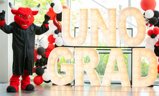 Durango standing next to a light up UNO Grad sign during commencement
