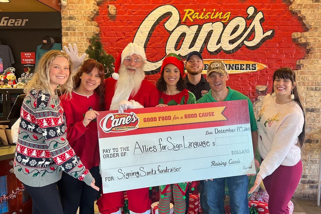 A group of people stand with Santa; they hold a giant fundraising check