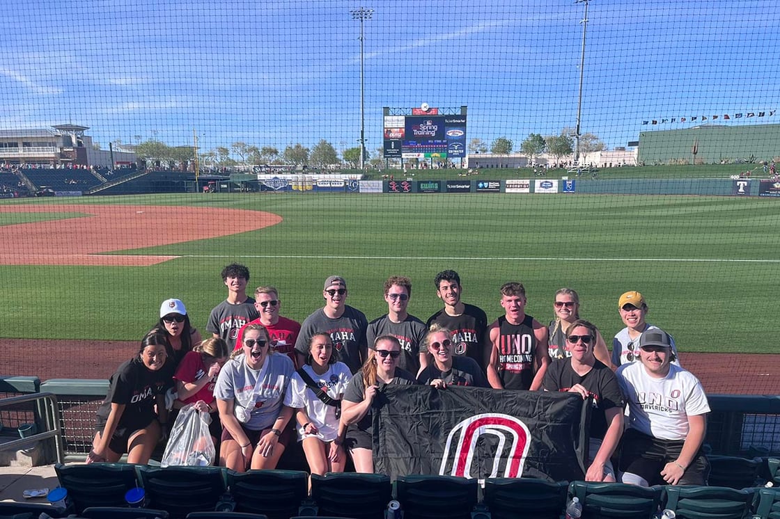 A group of people hold a UNO flag in a baseball stadium