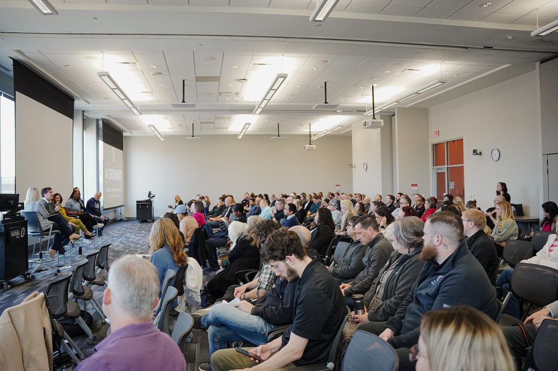 A wide-angle view of a packed room at the AI Summit, showing attendees listening to a panel discussion at the front of the room.