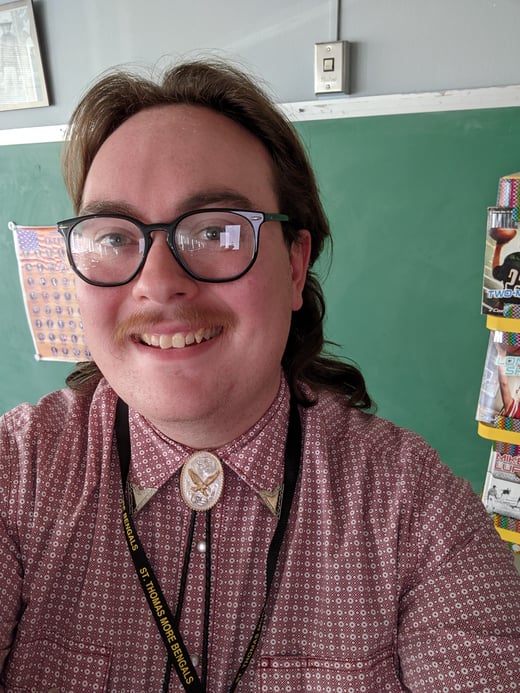 Jacob Domayer stands in front of a blackboard inside his classroom