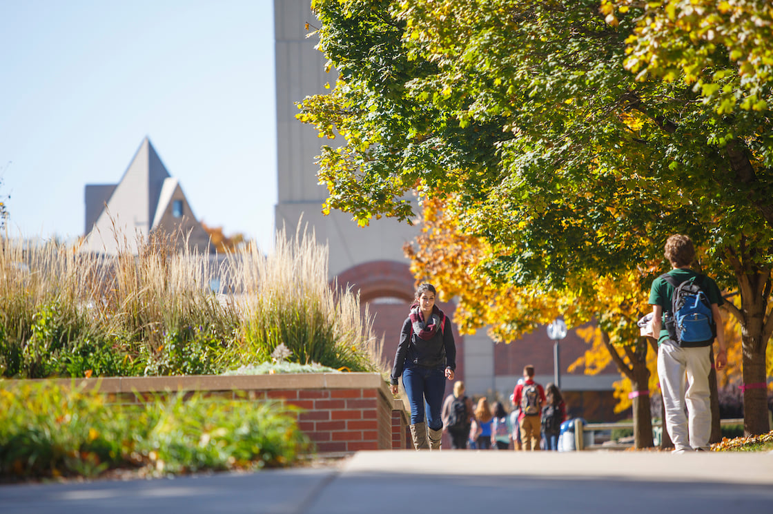 Students walking towards camera on UNO's campus with trees on the right-hand side changing colors