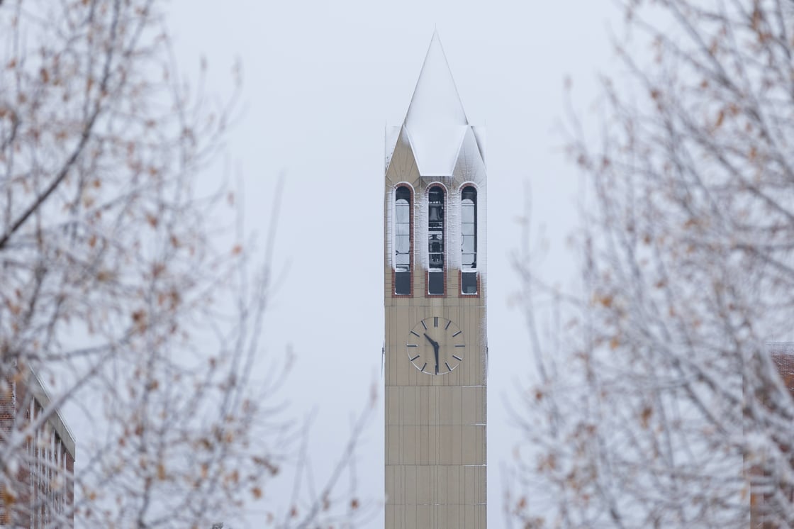 The UNO campanile covered in snow, framed by frost-covered tree branches on a gray winter day.