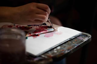 a hand holding a paint brush, stroking brush against white canvas with various water colors.