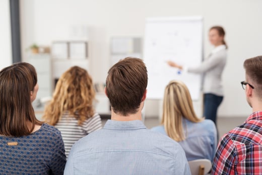 Rear View of Young Office Workers in Casual Outfits Listening to a Top Manager Explaining Something Using Illustrations.-1