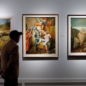 A visitor looks at paintings from Samuel Bak