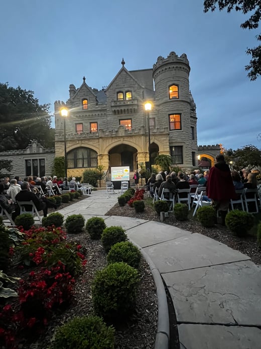 people are seated outdoors in chairs facing the Joslyn Castle